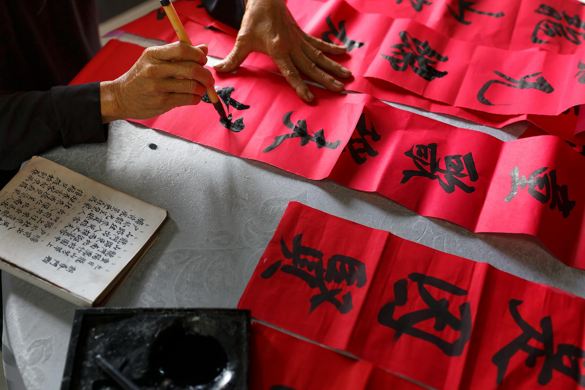 An artist creating Chinese calligraphy on red paper