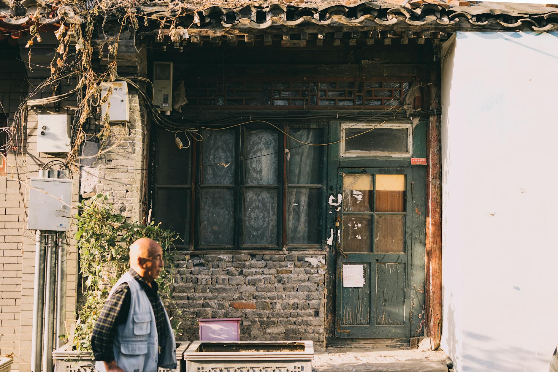Elderly man walking past a historic brick house in Beijing