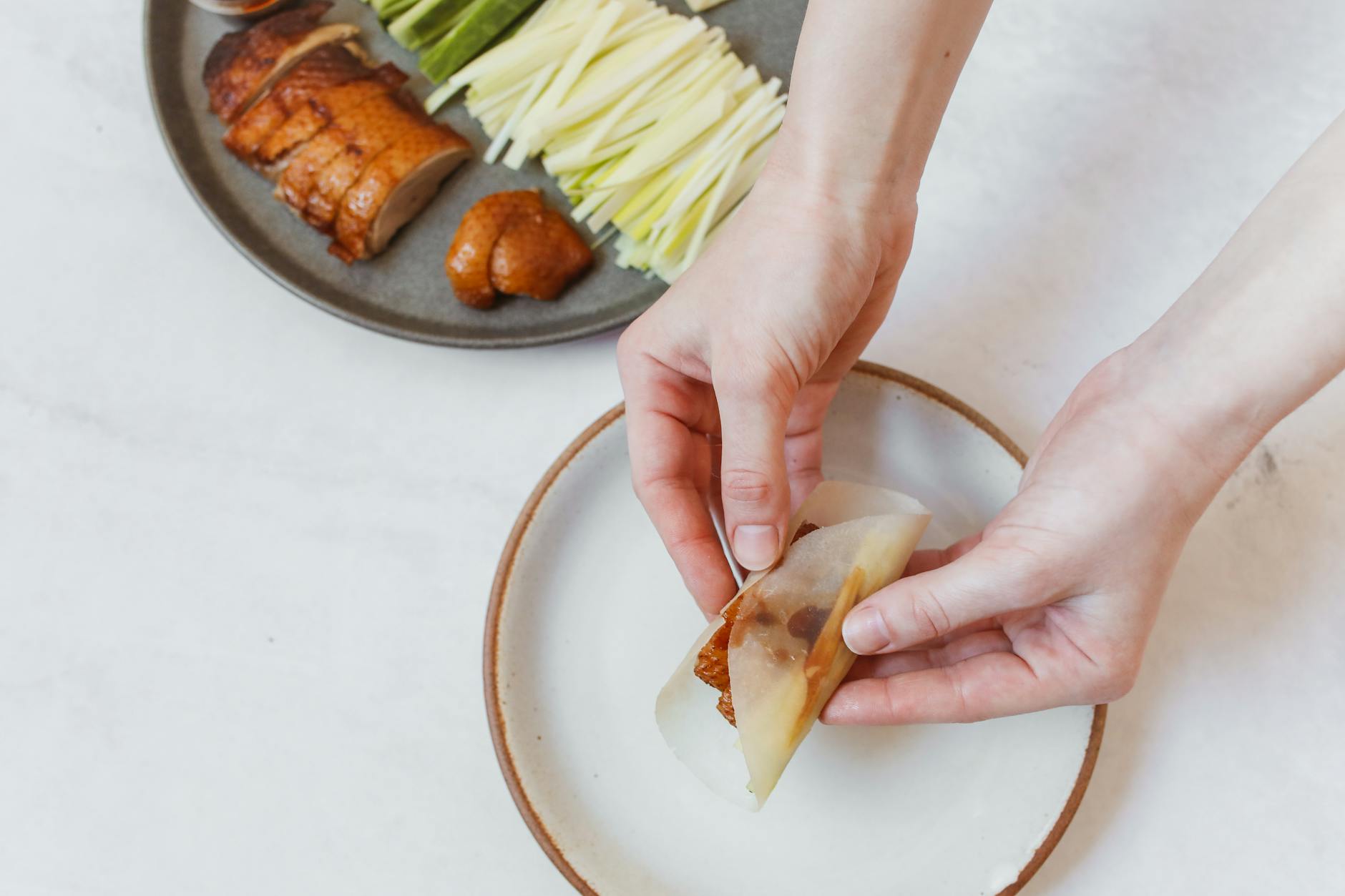 Hands wrapping Peking duck and vegetables in a thin pancake
