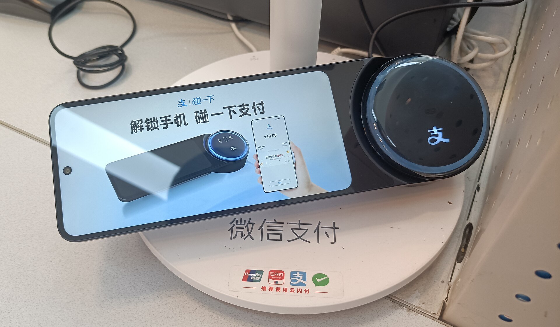 An Alipay tap-to-pay terminal on a shop counter, its base printed with UnionPay, Alipay and WeChat Pay logos