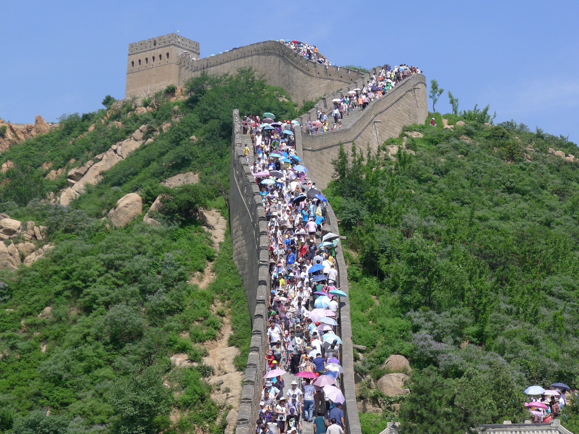 The Great Wall at Badaling packed shoulder to shoulder with visitors carrying parasols, filling the staircase from wall to wall