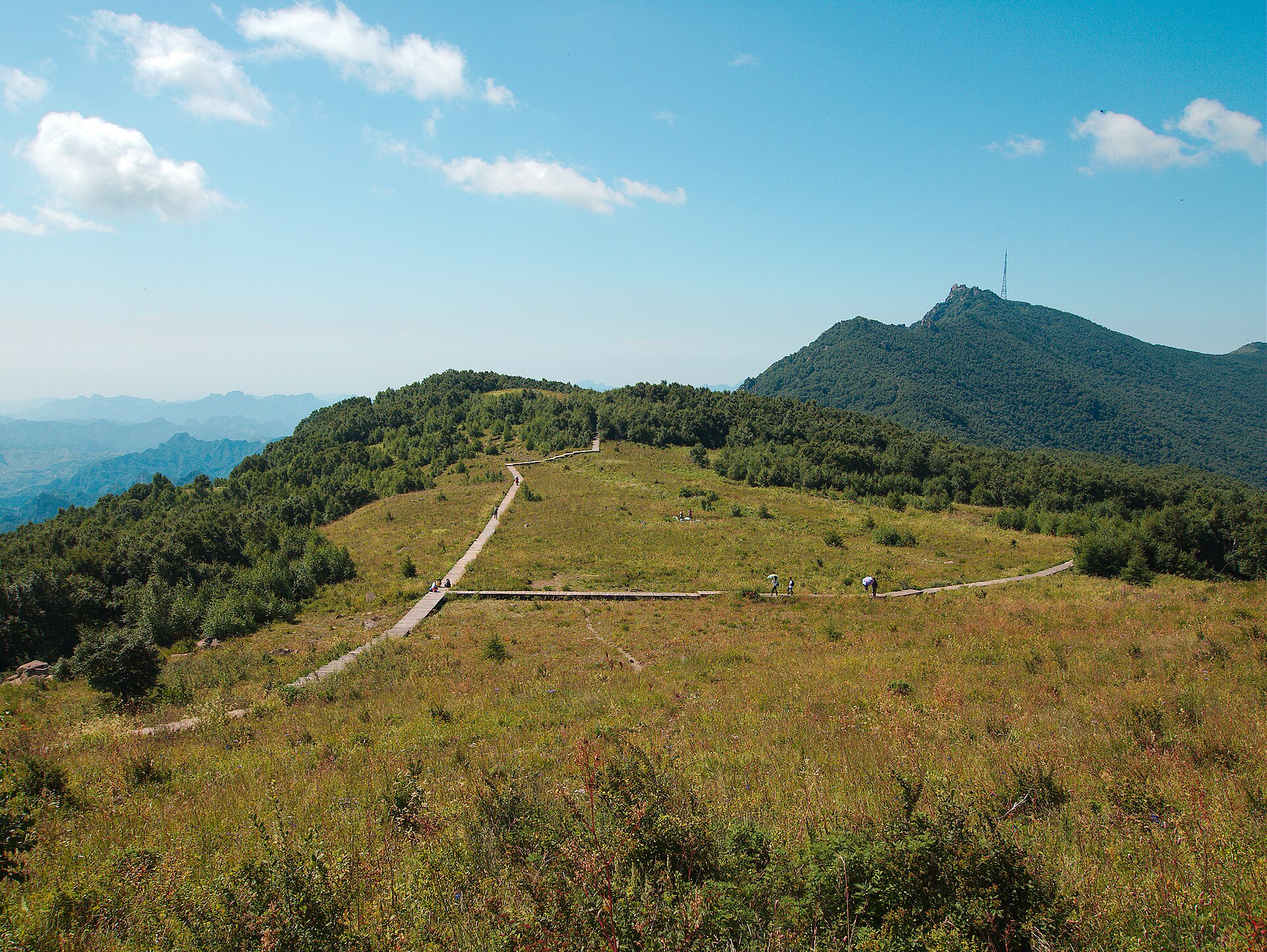 A boardwalk crossing the open alpine meadow on the summit plateau of Baihua Mountain near Beijing with forested ridges beyond