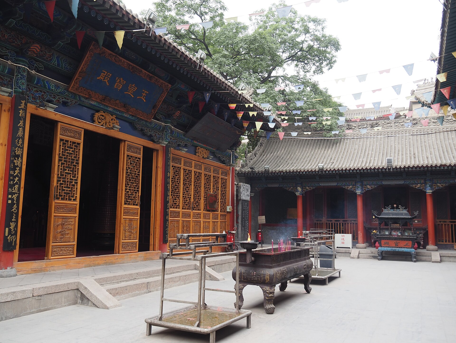 A quiet courtyard at the Baiyunguan Taoist temple in Beijing with incense burning in a bronze censer and prayer flags overhead
