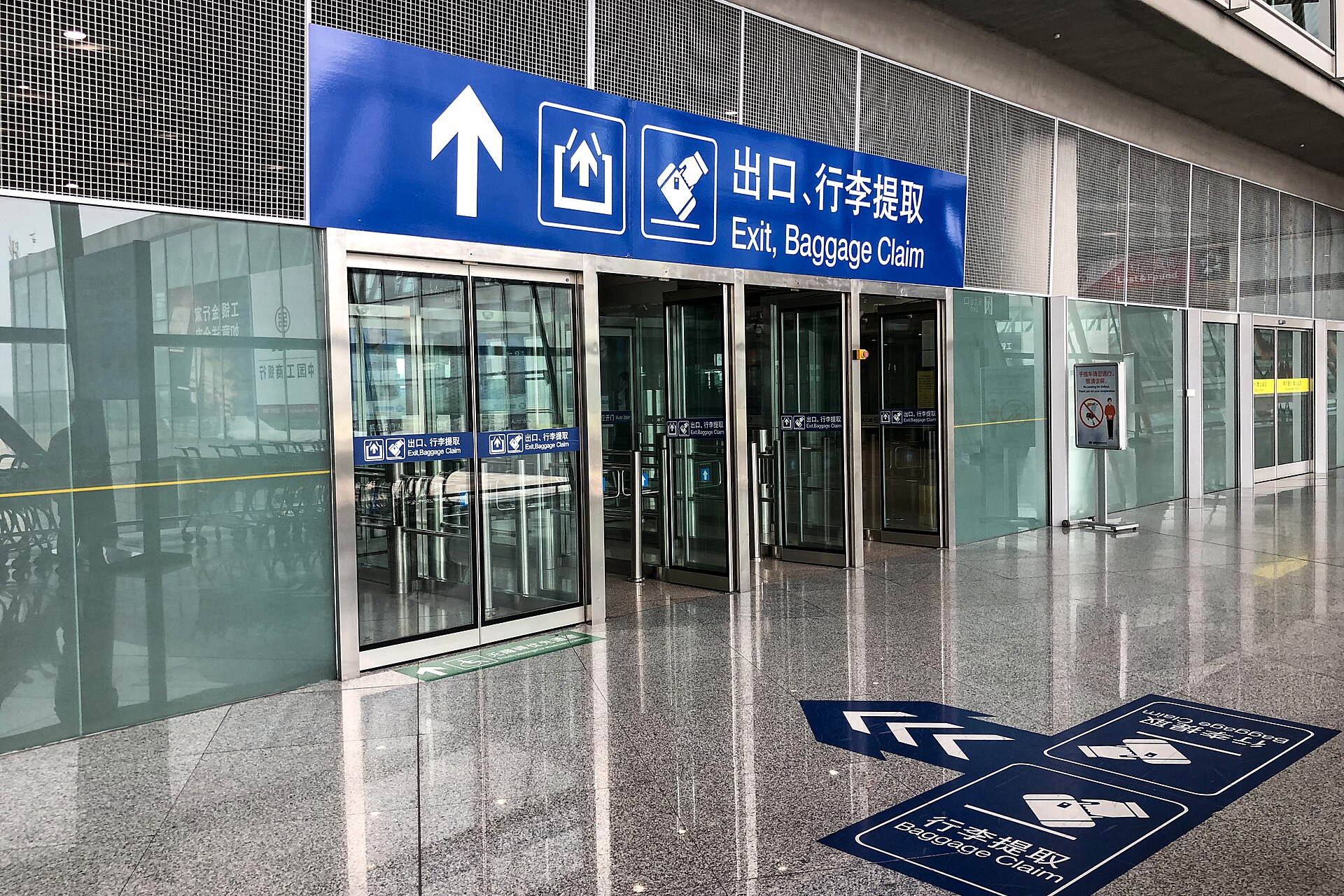 Glass exit doors under a blue sign reading Exit, Baggage Claim in the T3C arrival concourse at Beijing Capital International Airport
