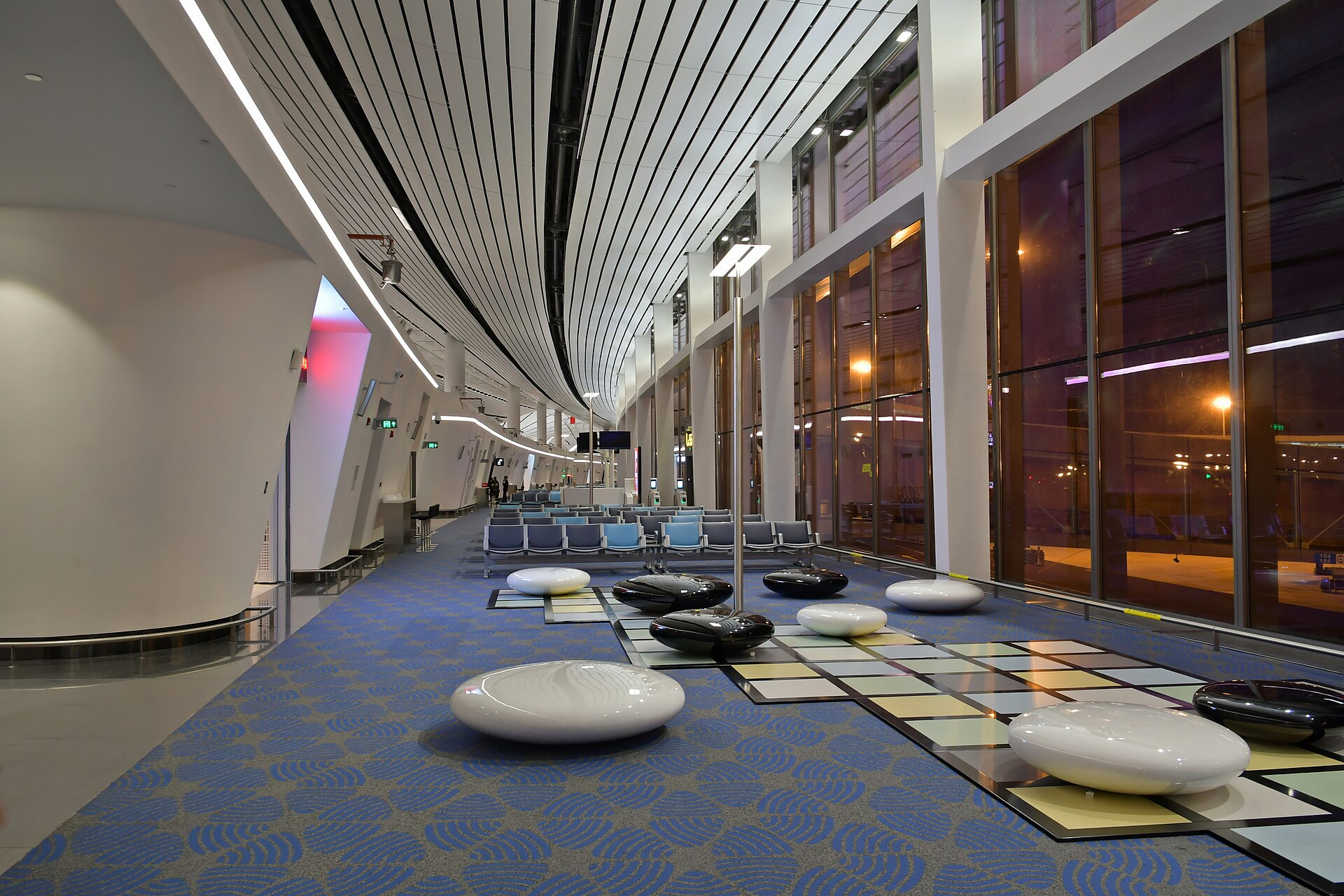 The curved interior of Beijing Daxing International Airport's terminal with seating and full-height windows at night