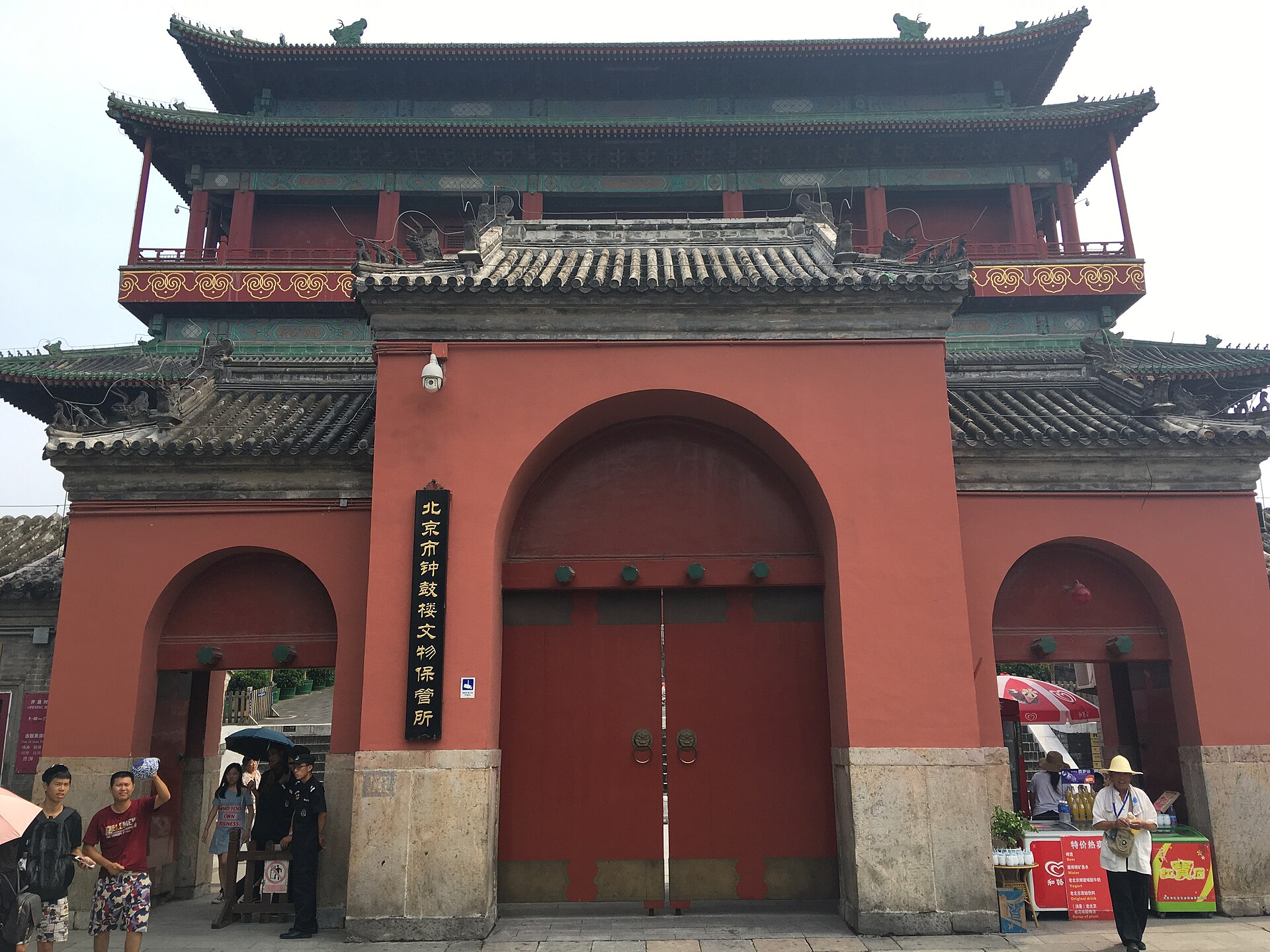 The red-walled base of the Beijing Drum Tower with arched gateways, upswept green-tiled eaves and a vertical Chinese signboard