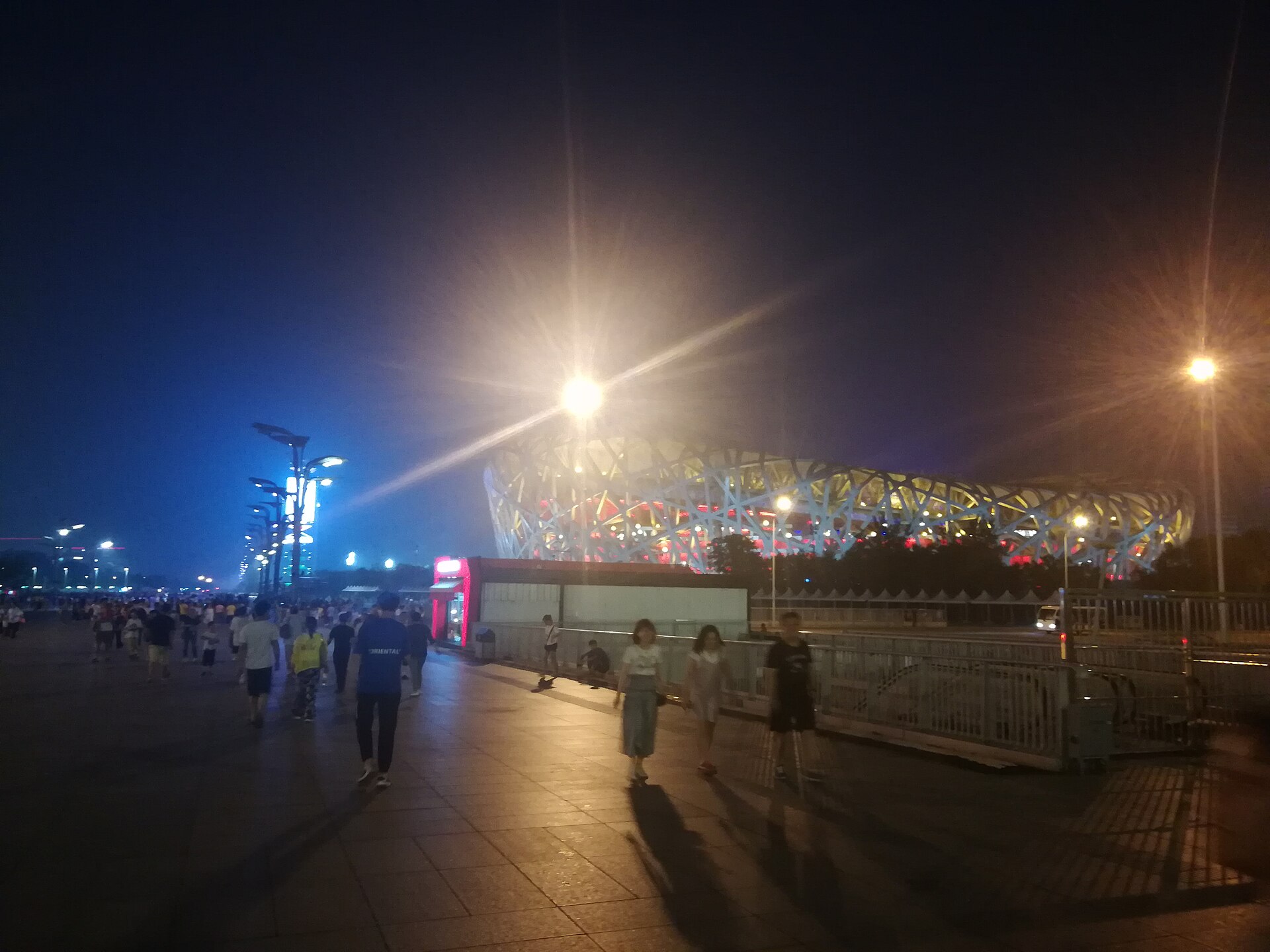 The Bird's Nest stadium lit at night in Beijing's Olympic Park with people walking along the promenade