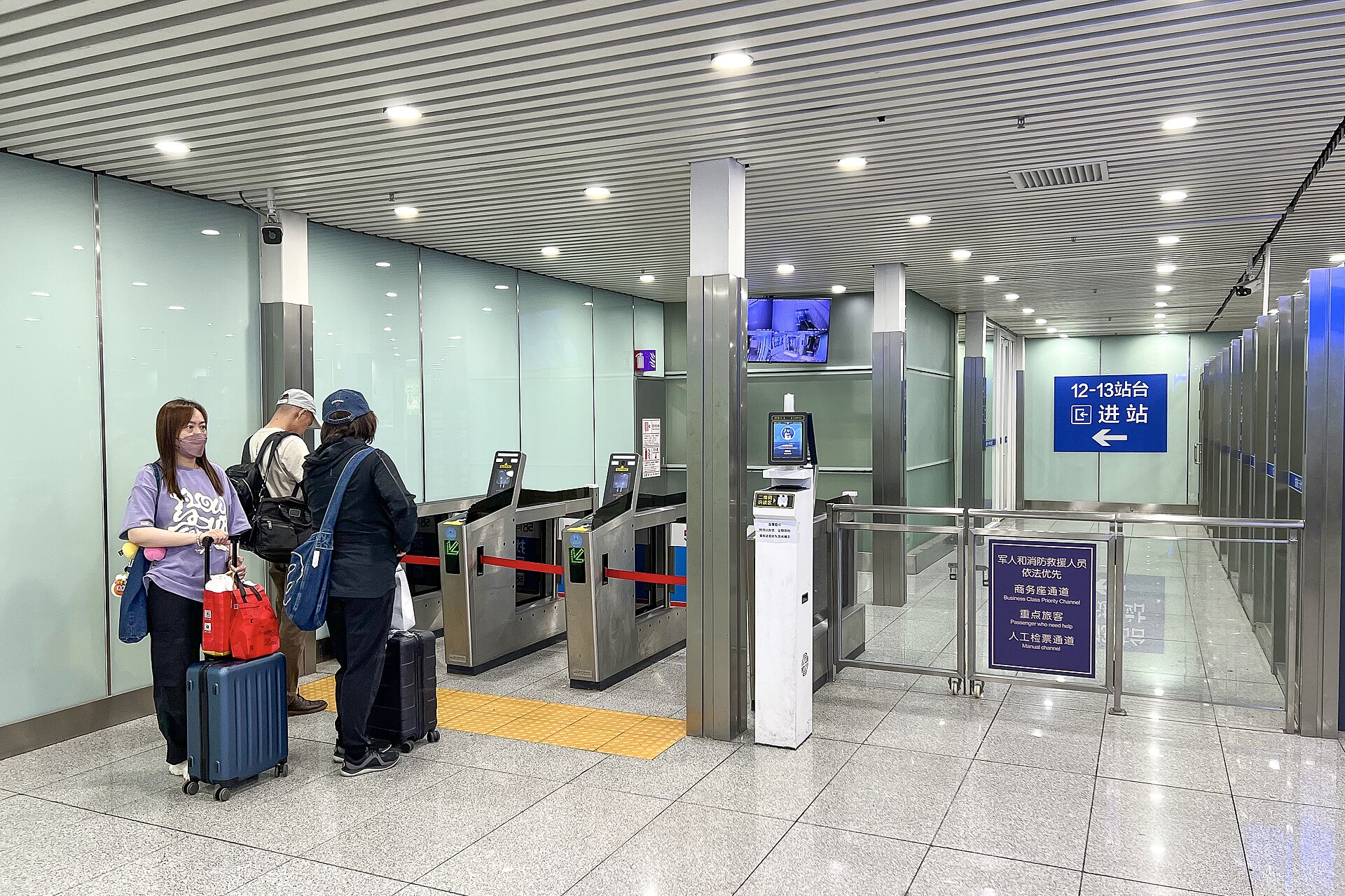 Travellers with suitcases at automatic ticket gates at Beijing South Railway Station, with a staffed manual channel to the right