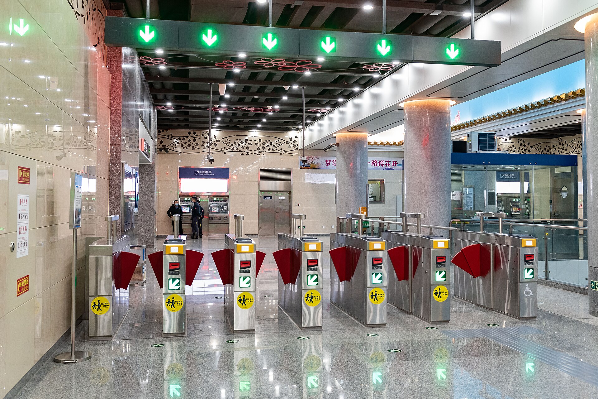 A row of stainless-steel subway faregates with red flaps and green arrow signals at Yuyuantan Park East Gate station in Beijing