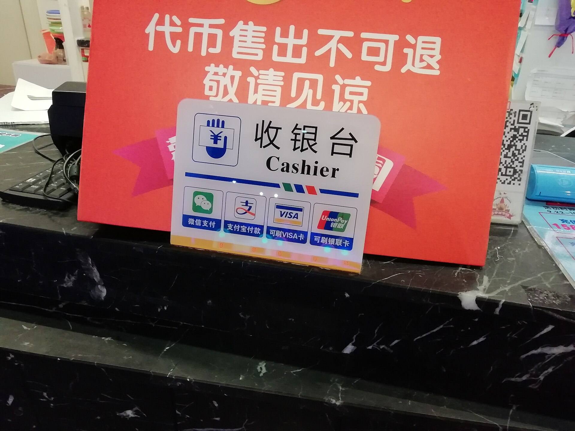 A cashier sign at a shop counter in China showing WeChat Pay, Alipay, Visa and UnionPay logos
