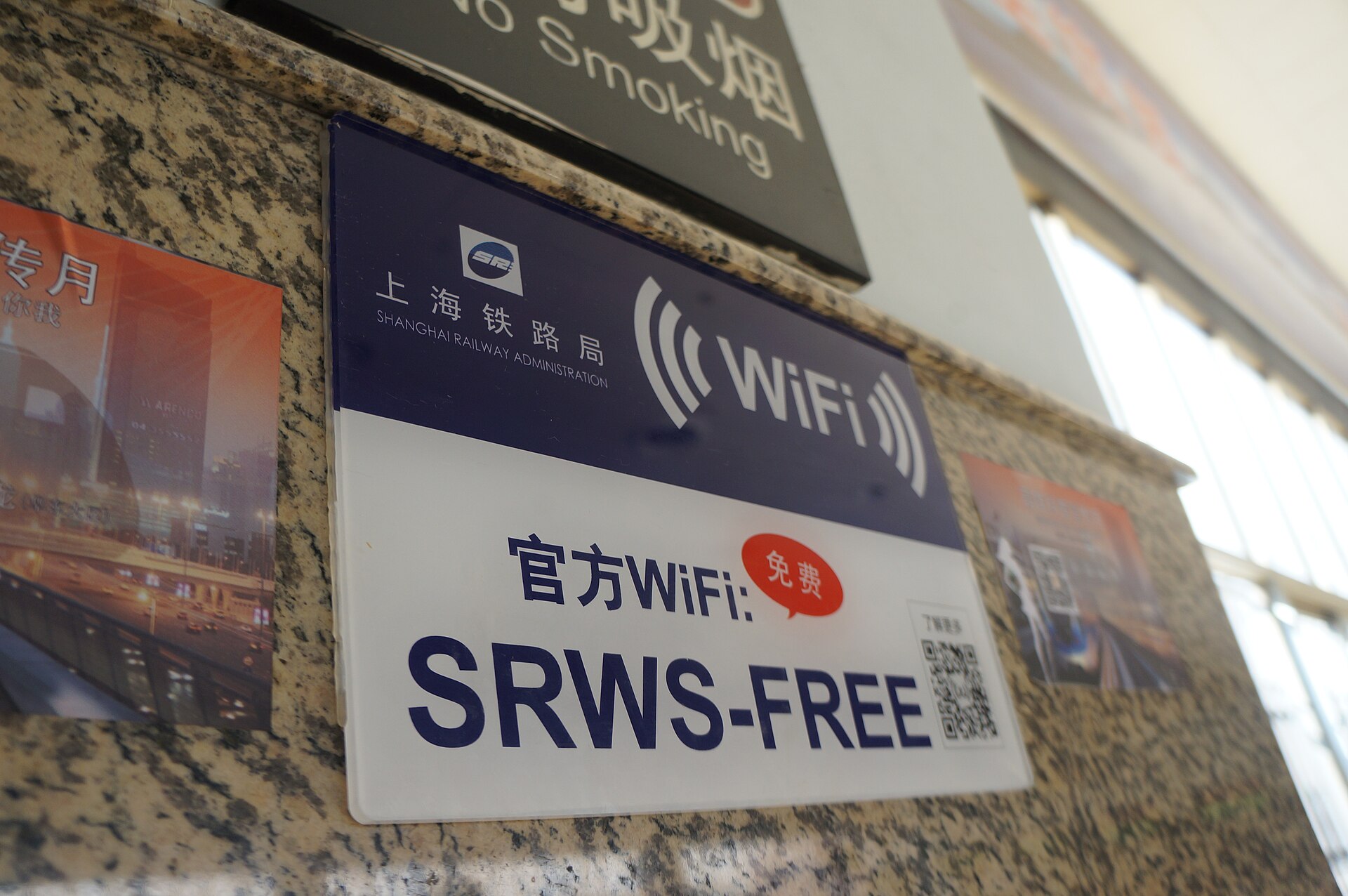 A blue and white sign on a stone wall at a Chinese railway station advertising free official WiFi named SRWS-FREE, with a QR code