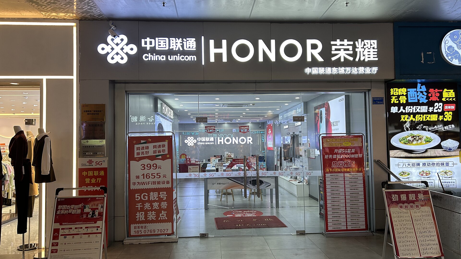 A China Unicom business hall entrance in a shopping mall, with red signs and boards listing phone numbers for sale