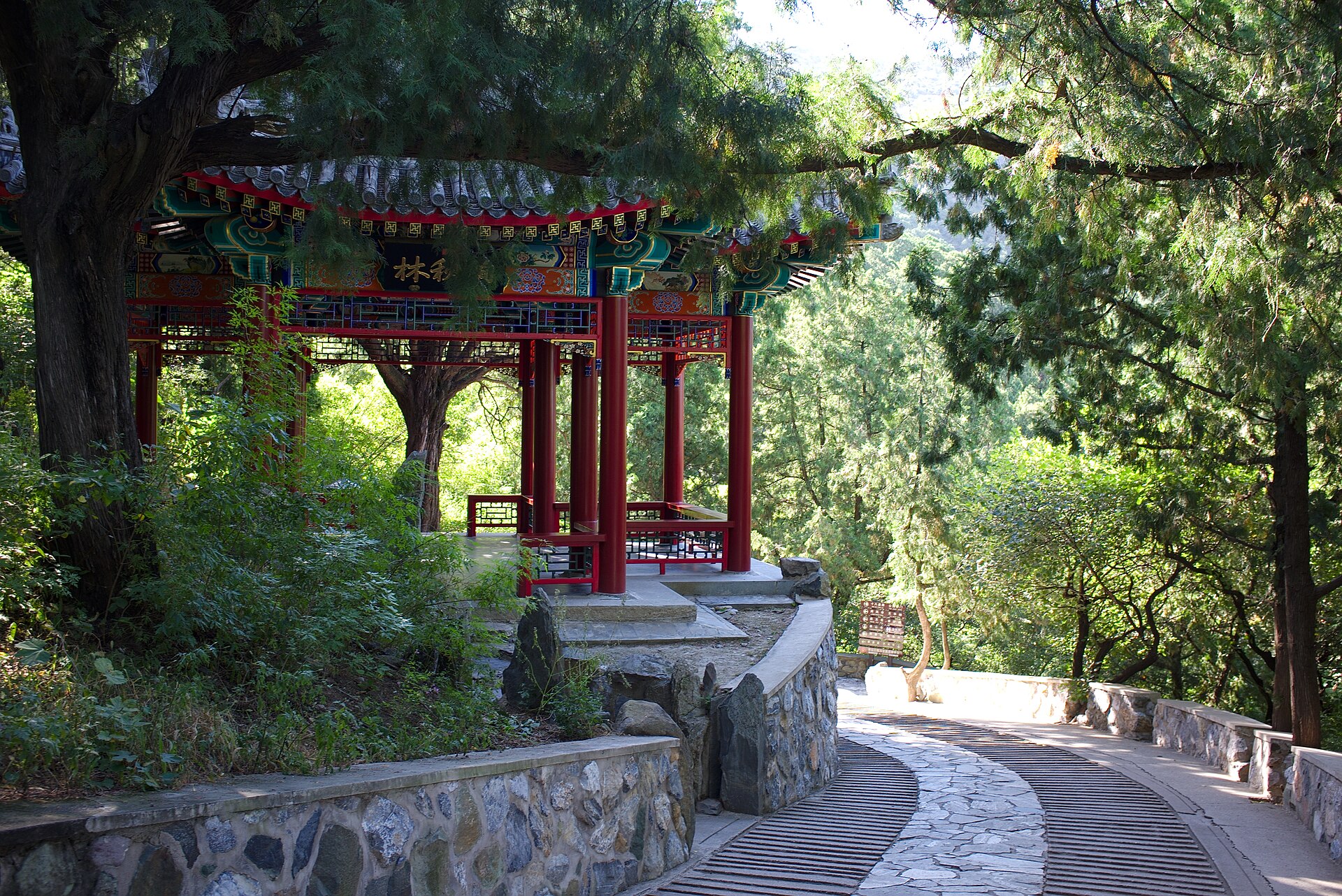 A painted pavilion beside a paved stepped path winding through pine woods at the Fragrant Hills near Beijing