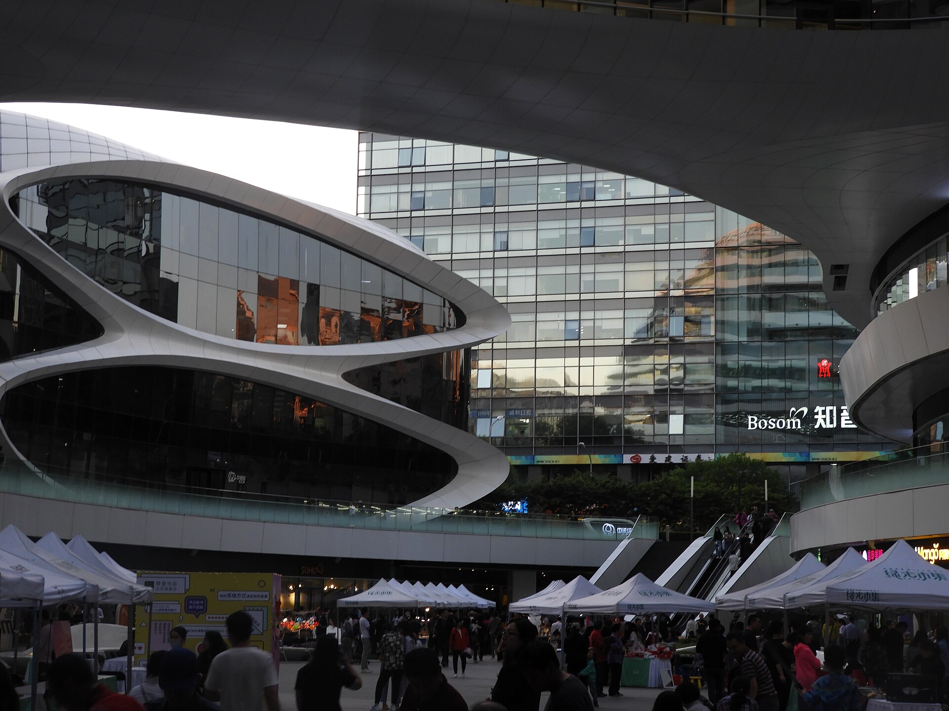 The curved white shells and stacked atrium bridges of Galaxy SOHO in Beijing seen from the public plaza below
