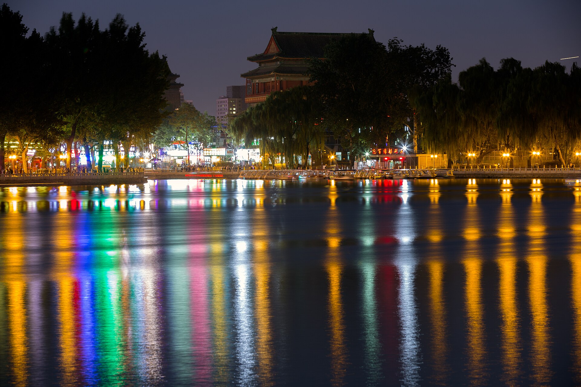 Houhai lake at night with coloured lights reflected on the water and the Drum Tower lit behind the willows