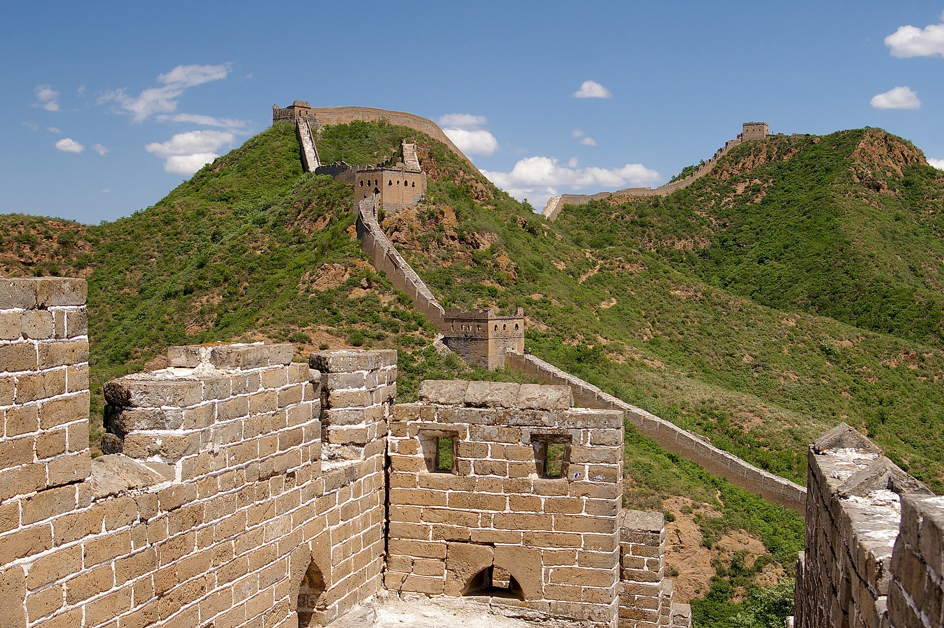 Ruined watchtowers of the Jinshanling Great Wall receding along a series of green ridges under a blue sky