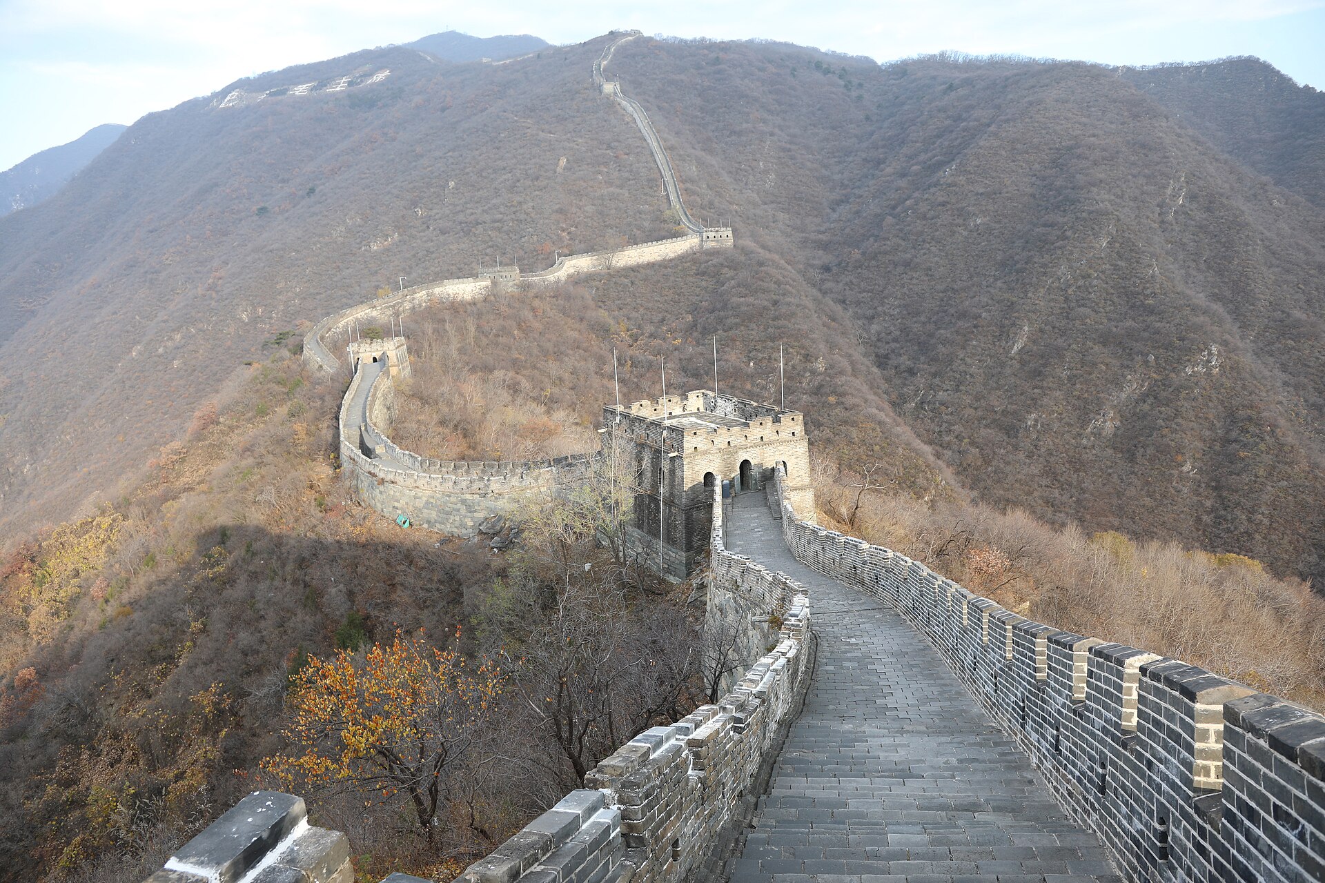 The wide paved walkway of the restored Mutianyu Great Wall with high brick parapets on both sides curving between watchtowers