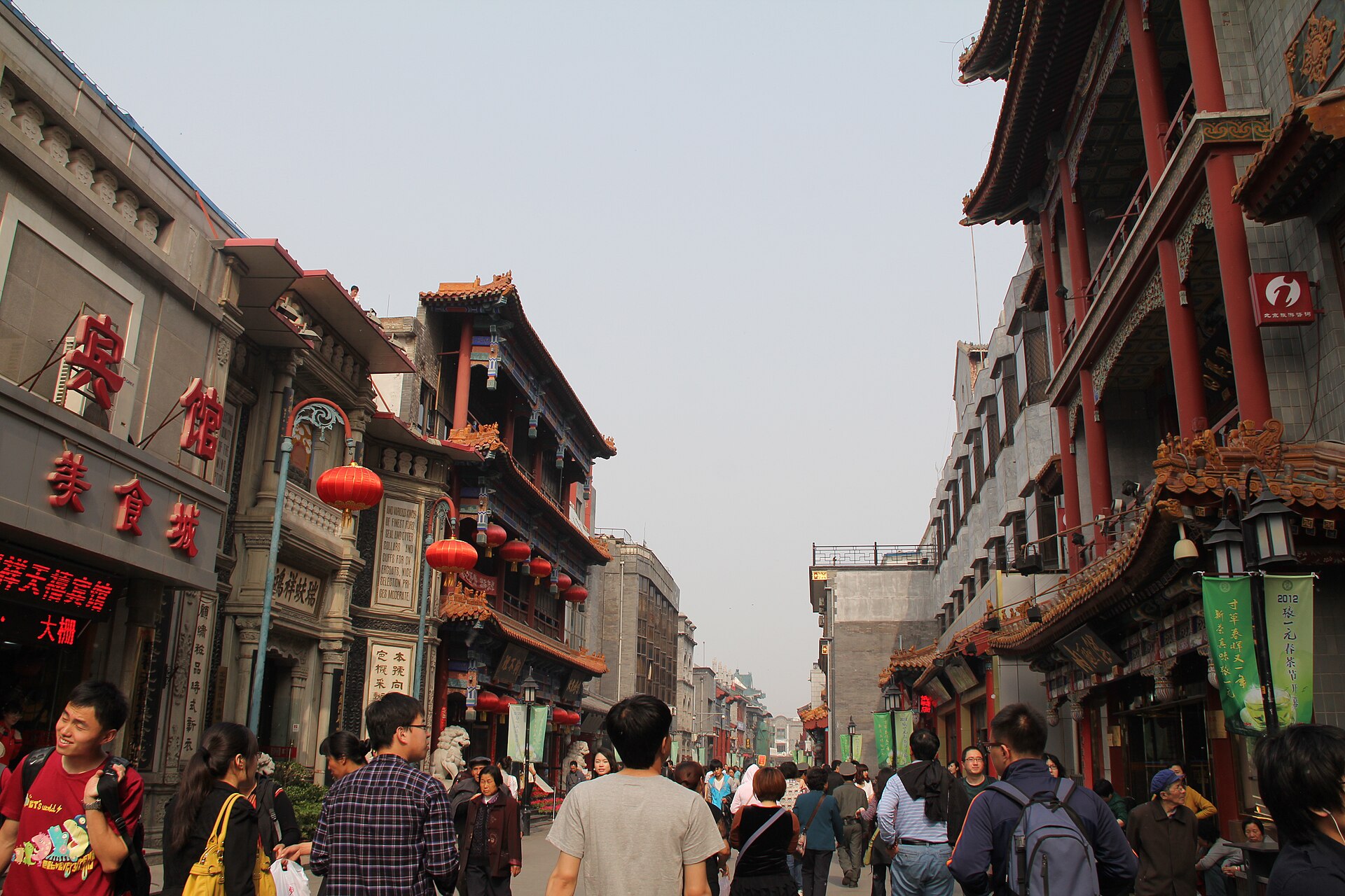 Restored shopfronts with red lanterns and traditional signage along a crowded pedestrian street at Qianmen in Beijing
