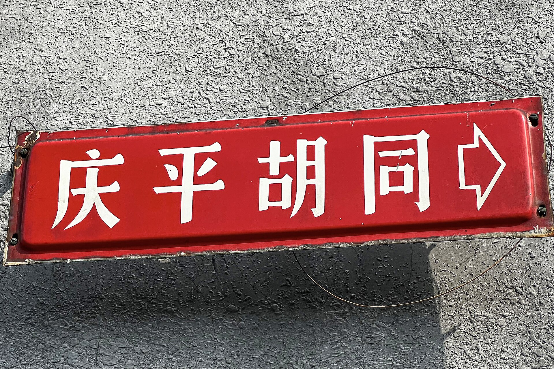 A red enamel street sign with white Chinese characters reading Qingping Hutong and an arrow pointing right, fixed to a grey rendered wall