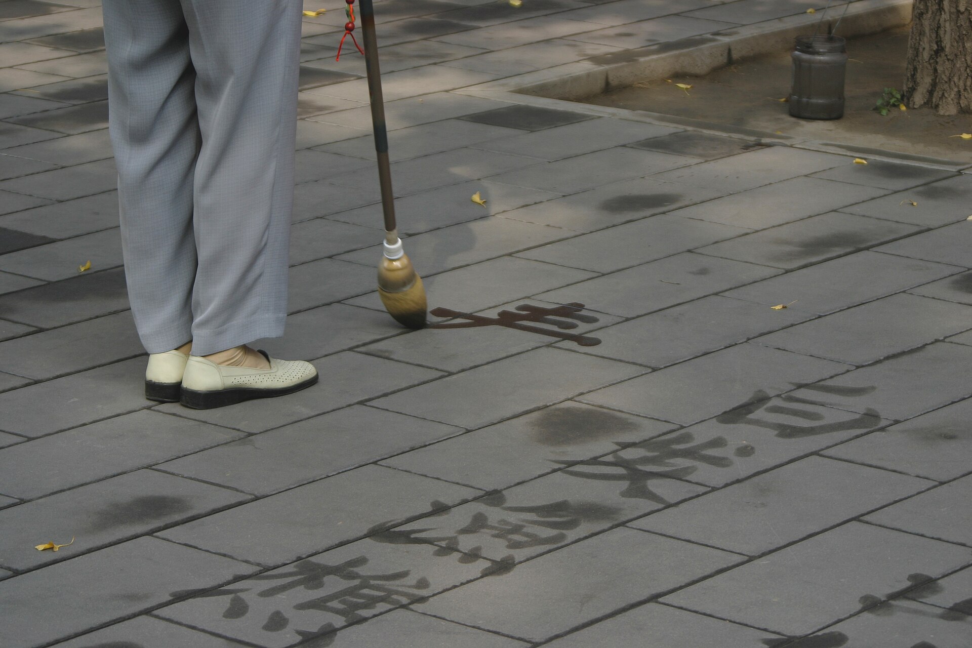 A man writing large Chinese characters on stone paving with a long brush dipped in water in Jingshan Park