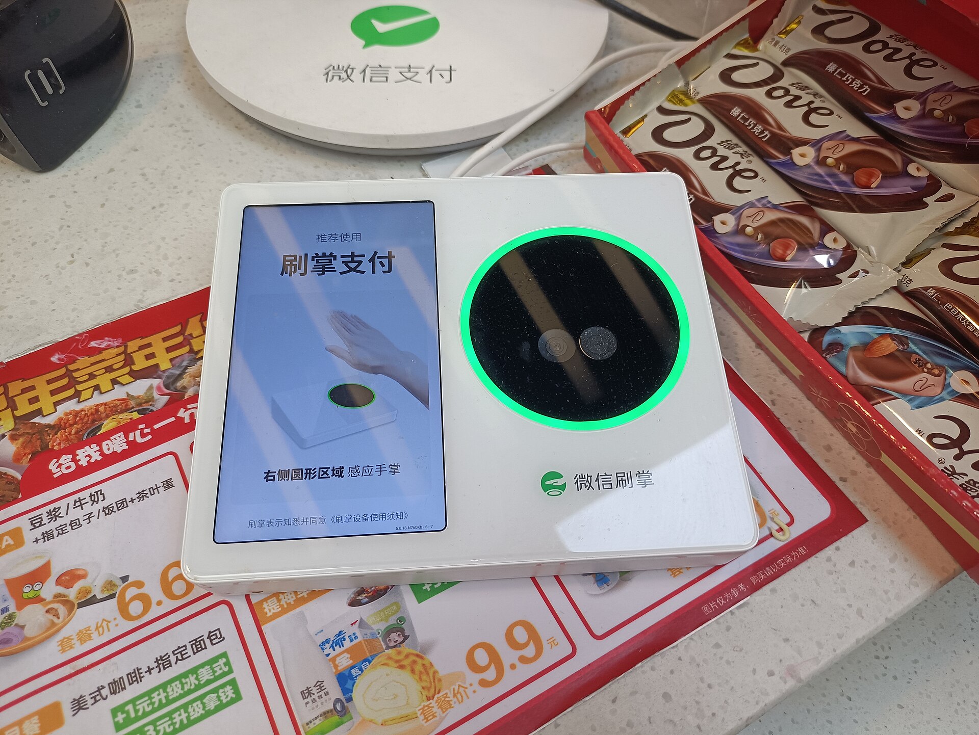 A WeChat palm-payment terminal with a glowing green sensor ring beside a WeChat Pay stand on a shop counter