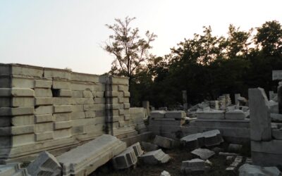 Carved white marble blocks and a broken wall among trees at the Western Mansions ruins in Yuanmingyuan