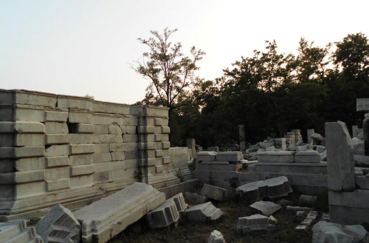 Carved white marble blocks and a broken wall among trees at the Western Mansions ruins in Yuanmingyuan