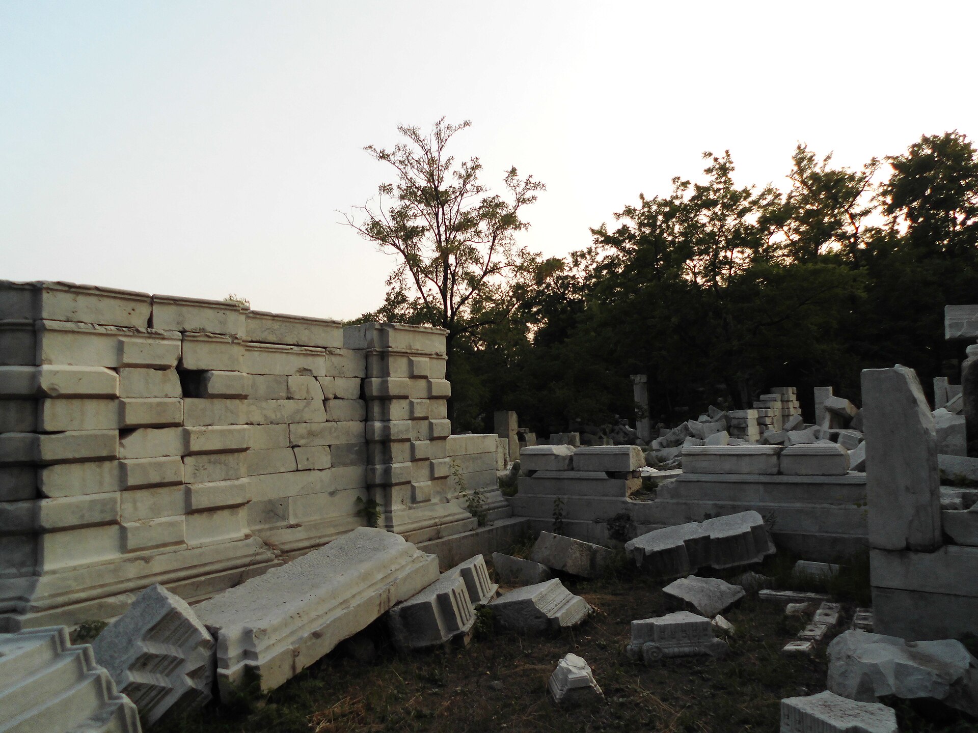 Carved white marble blocks and a broken wall among trees at the Western Mansions ruins in Yuanmingyuan
