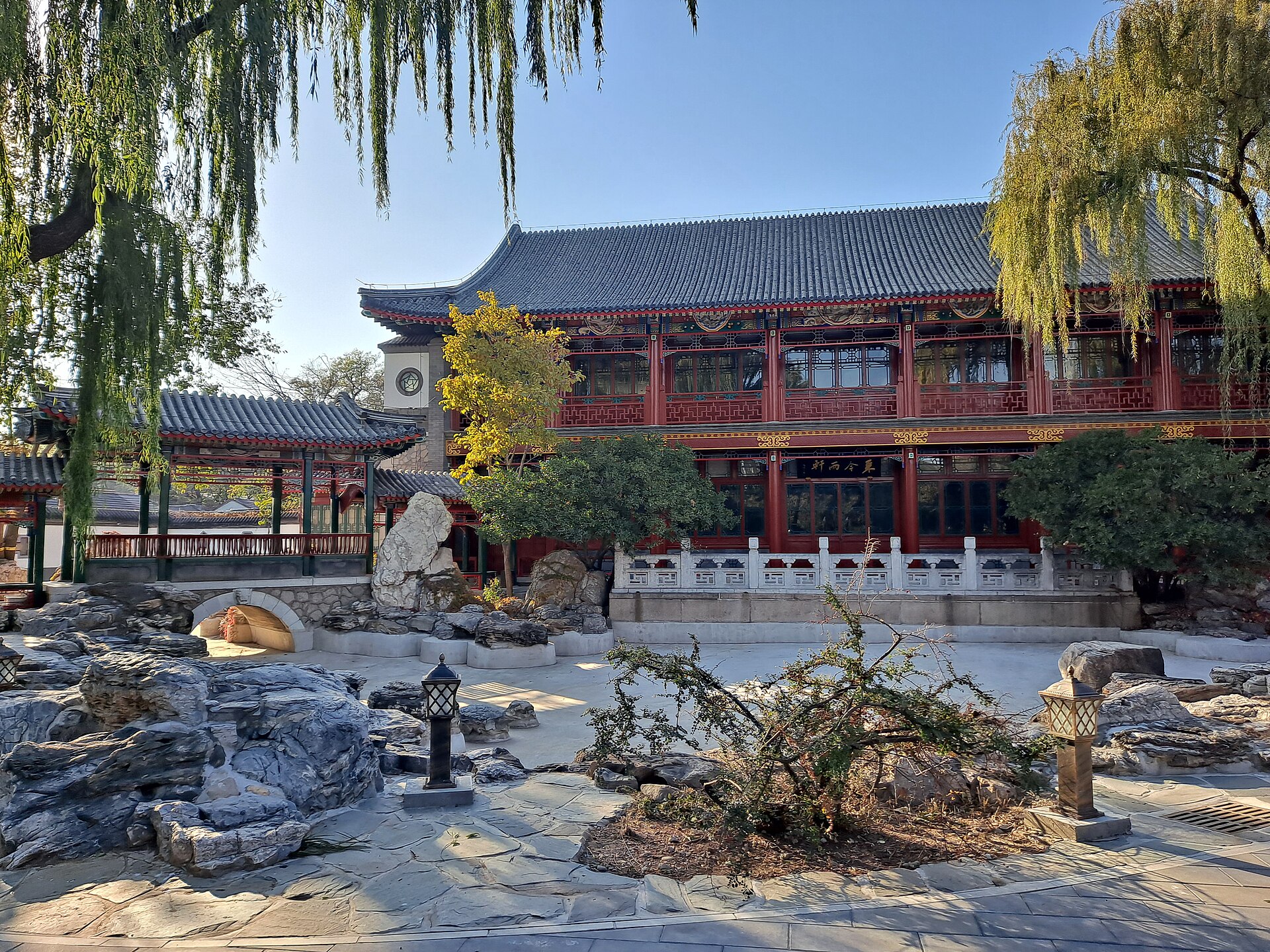 A two-storey red-pillared hall with grey tiled roofs behind a rockery and willow trees in Zhongshan Park, Beijing