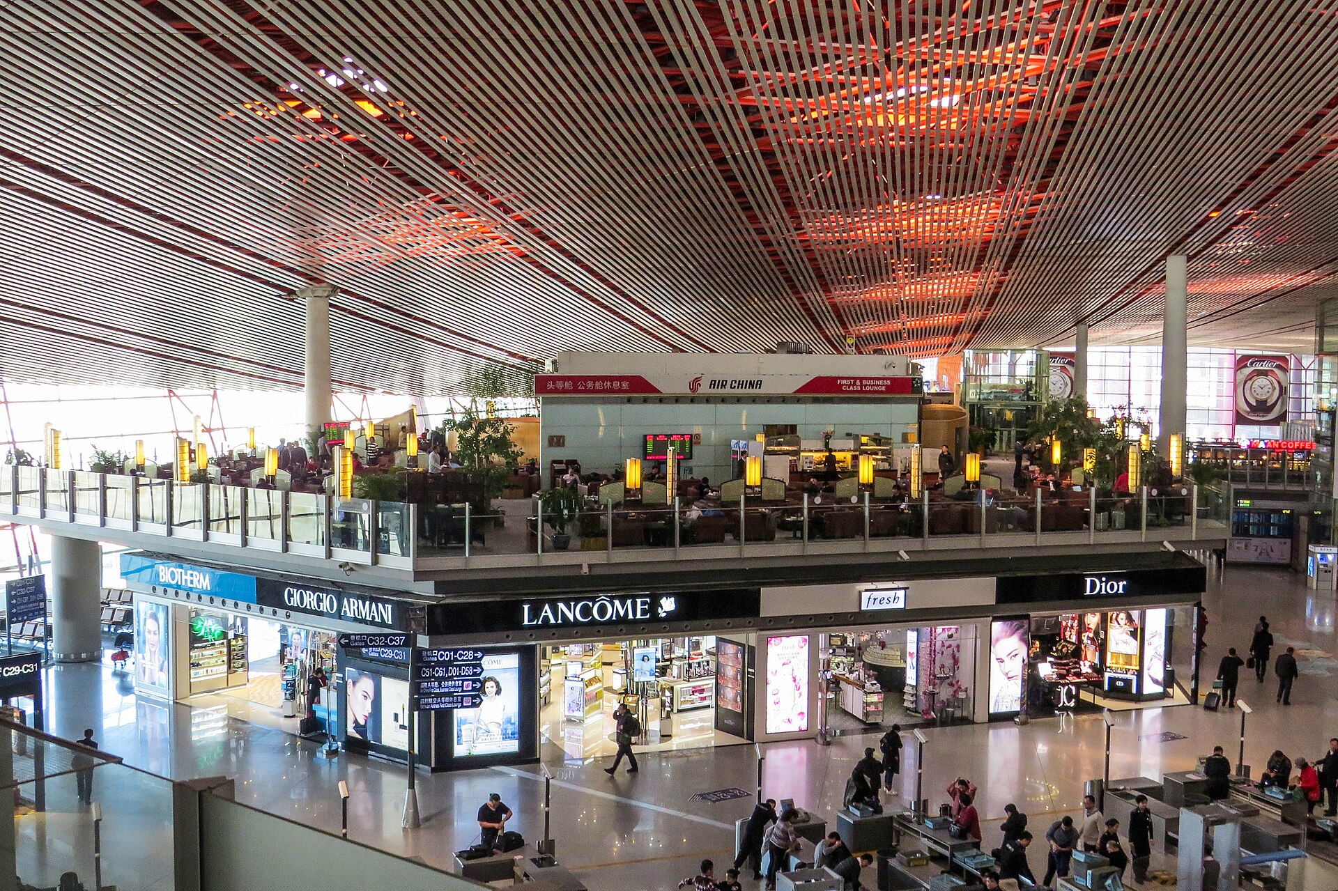 An Air China first and business class lounge overlooks shops and passengers beneath Beijing Capital Airport Terminal 3-C ceiling.