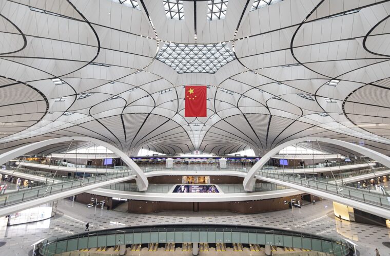 Beijing Daxing Airport has a sweeping white ceiling above several open terminal levels, with a Chinese flag hanging centrally.