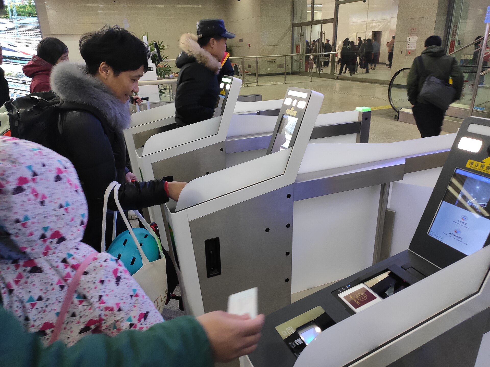 Passengers passing through automatic ticket gates at Beijing North railway station, with a passport reader marked on the nearest machine