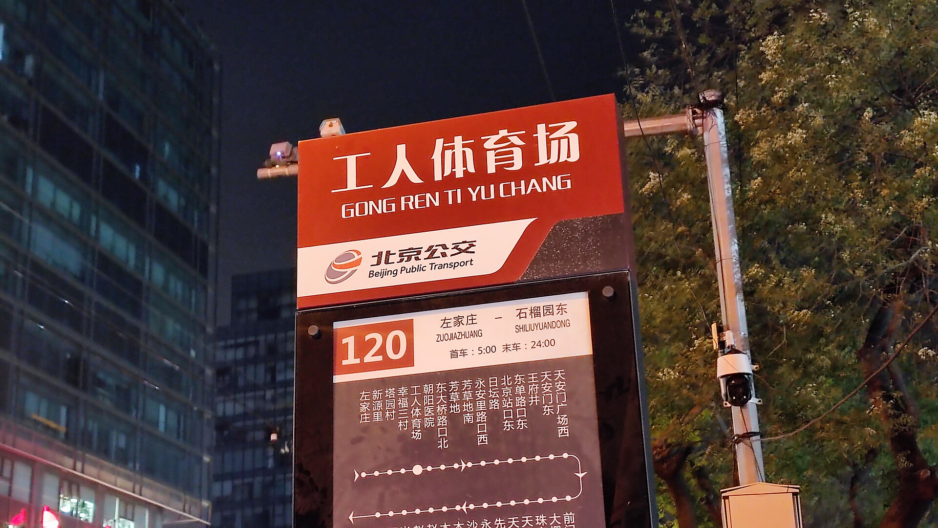 Beijing Workers' Stadium bus stop board at night displays route 120, operating hours and a diagram of stops.
