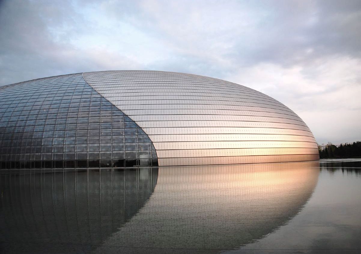 Beijing's National Centre for the Performing Arts curves above a still pool, with its metal and glass facade reflected in the water.