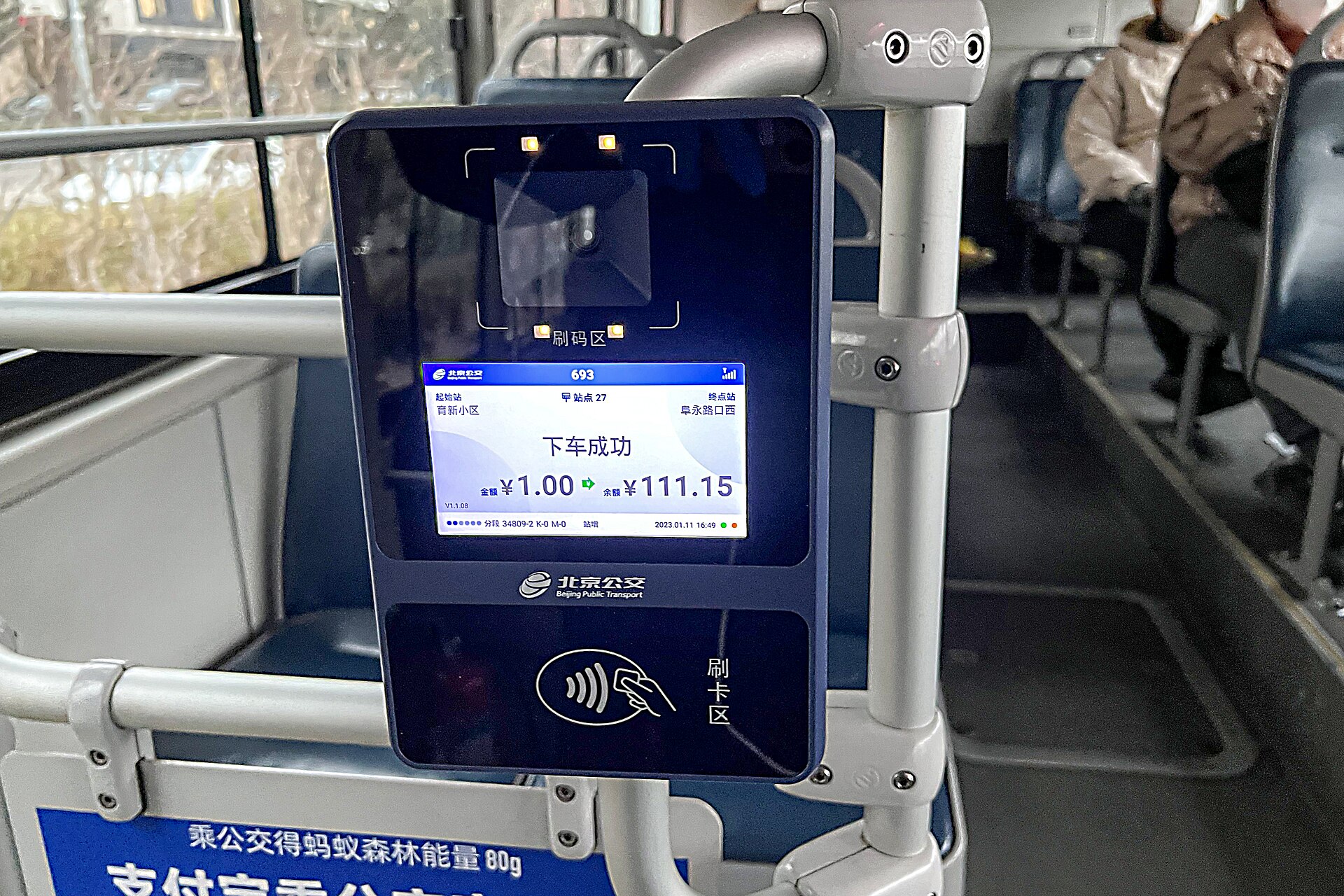 A blue Beijing bus card reader displays a successful transaction beside the rear doorway, with seated passengers behind it.