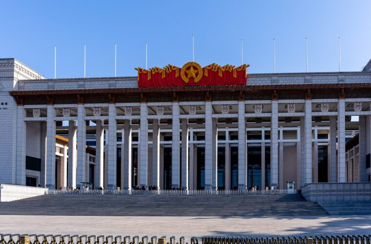 Broad steps lead to the National Museum of China's tall stone colonnade in Beijing beneath a clear blue sky.