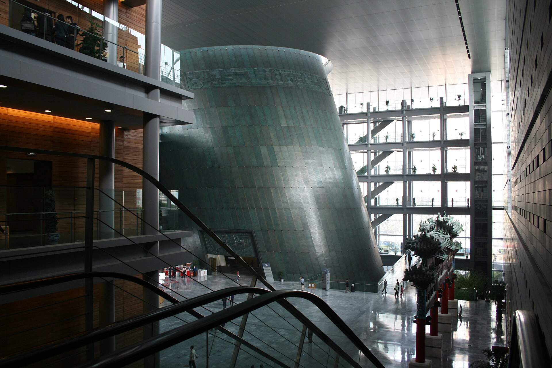The atrium of the Capital Museum in Beijing, with a huge tilted bronze-clad drum rising through the space and a painted memorial archway on the right