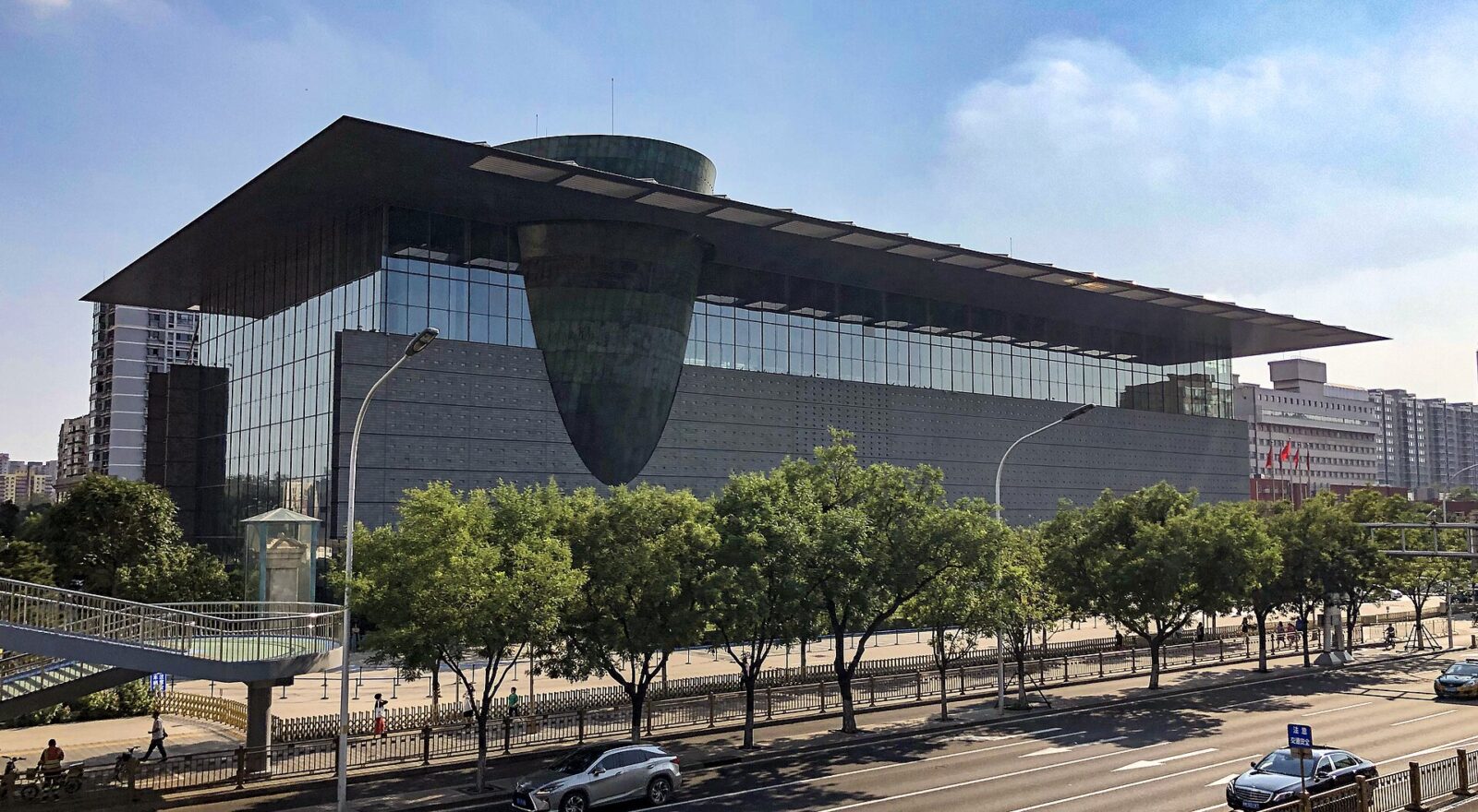The Capital Museum in Beijing, a glass-walled building under a wide overhanging roof, with a bronze-clad drum tilting out through the facade