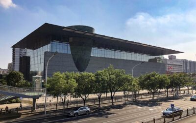 The Capital Museum in Beijing, a glass-walled building under a wide overhanging roof, with a bronze-clad drum tilting out through the facade