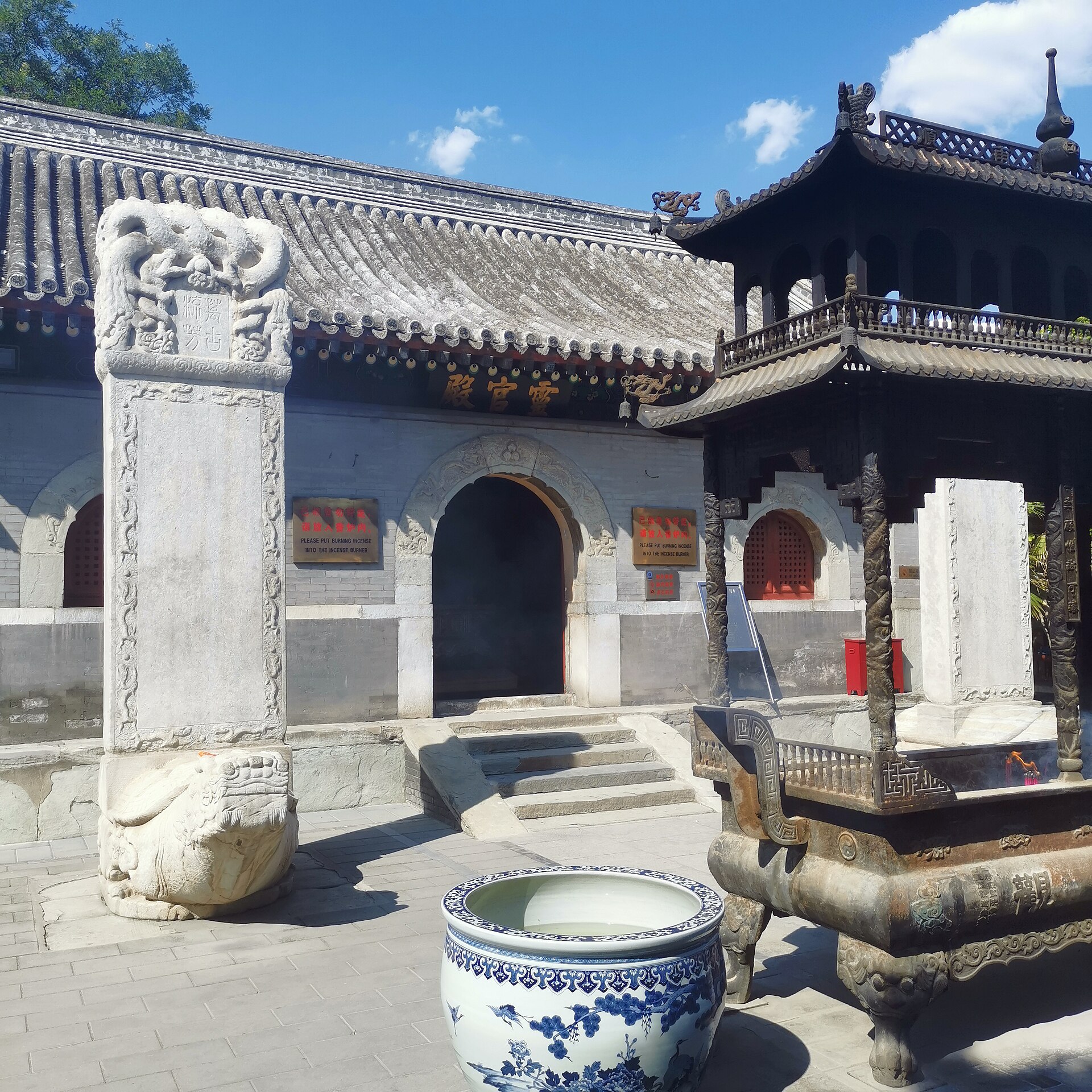 A carved stone stele and bronze incense burner stand before grey-tiled Lingguan Hall at Beijing's White Cloud Temple.