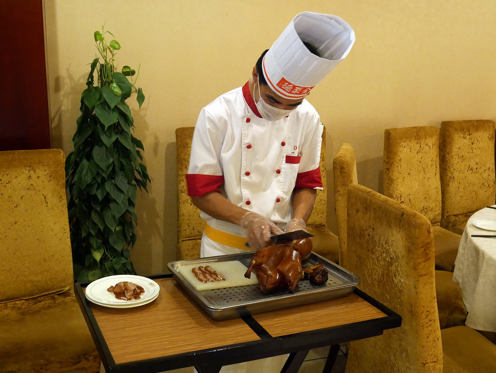 A chef at Quanjude in Beijing slices a glossy roast duck on a trolley beside a plate of carved meat.