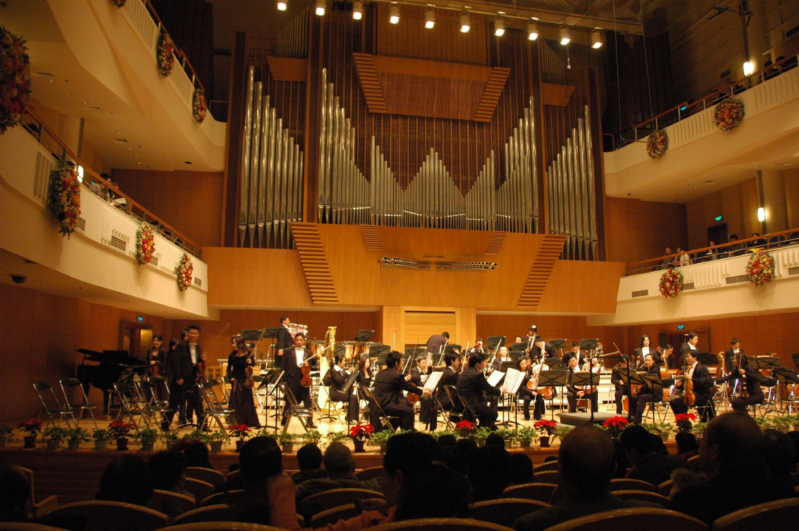 The China Philharmonic Orchestra on stage beneath the pipe organ at Beijing Concert Hall, with seated audience members in front.