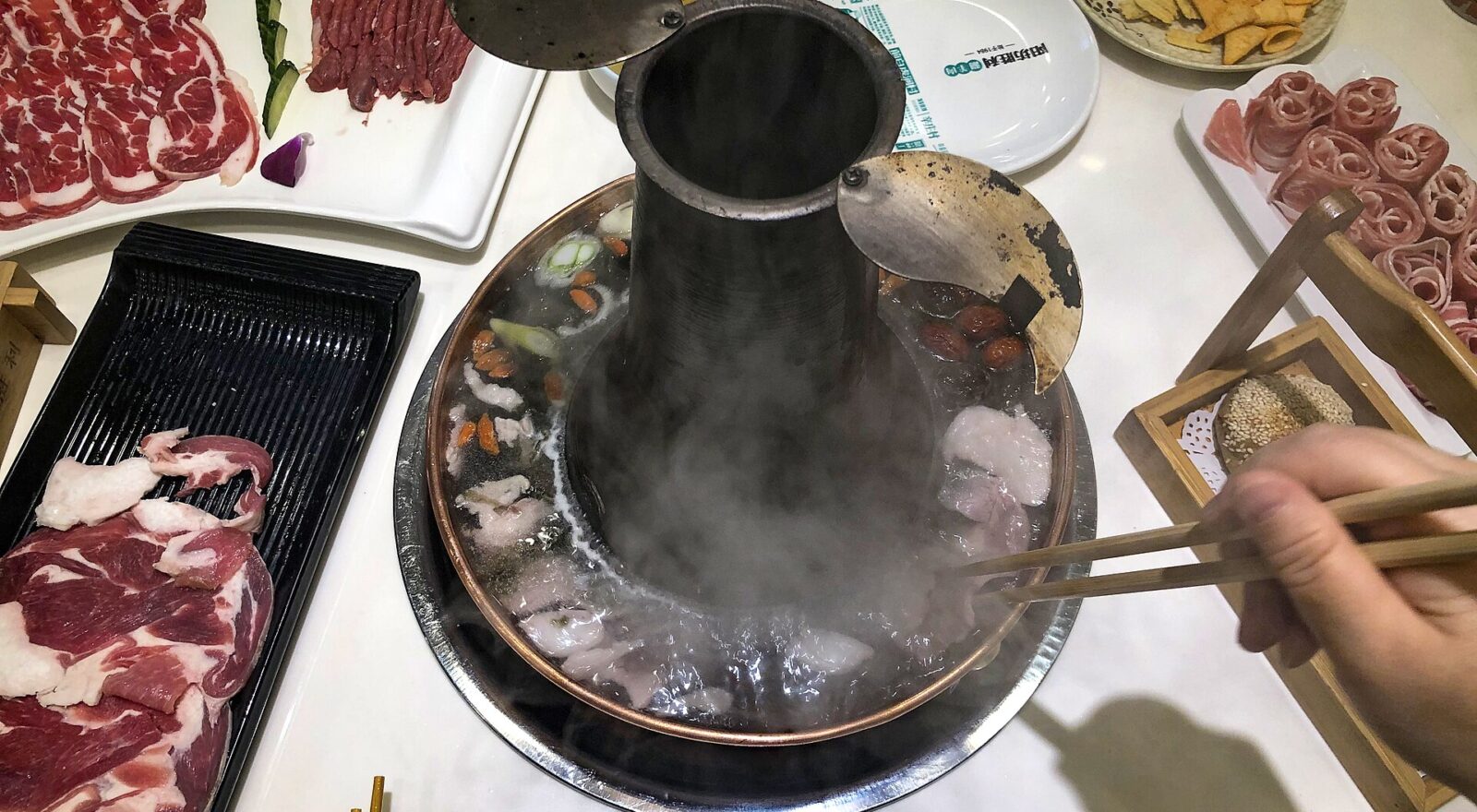 Chopsticks lower thin lamb slices into a steaming copper chimney hot pot at Yangfang Shengli in Beijing.