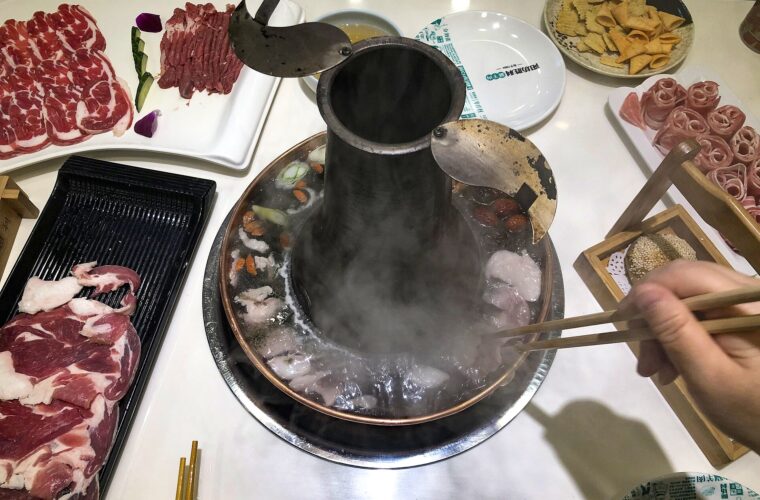 Chopsticks lower thin lamb slices into a steaming copper chimney hot pot at Yangfang Shengli in Beijing.