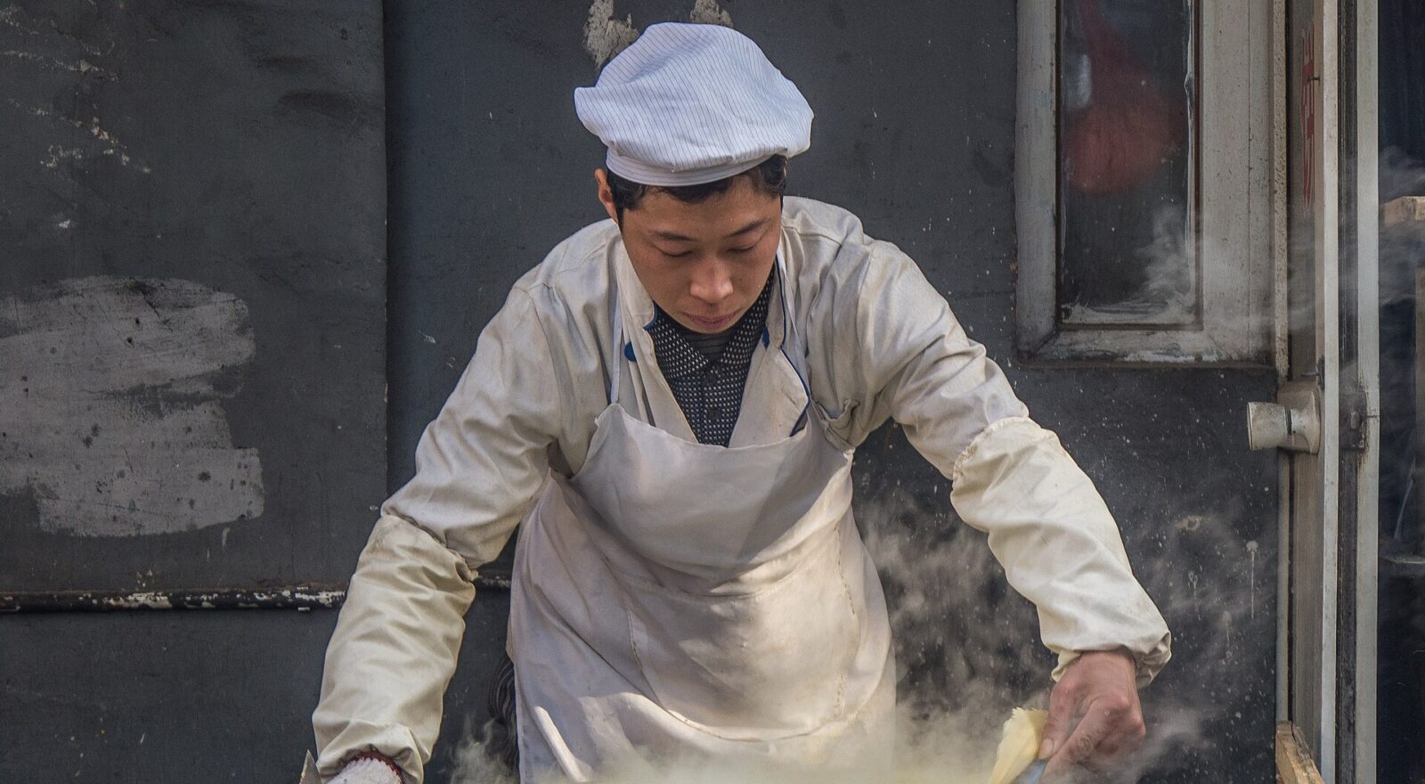 A cook lifts a thin pancake from a steaming round griddle at a food shop in Xicheng, Beijing.