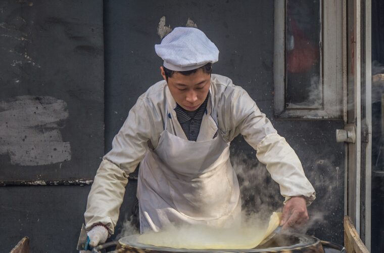 A cook lifts a thin pancake from a steaming round griddle at a food shop in Xicheng, Beijing.