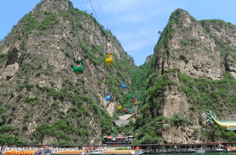 Covered tour boats line the reservoir beneath steep cliffs and colourful cable cars at Longqing Gorge in Beijing.