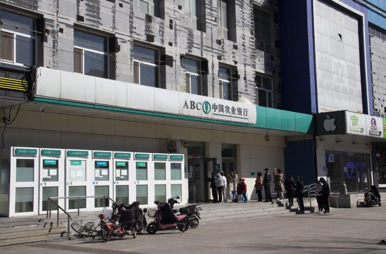 Customers queue outside an Agricultural Bank of China branch in Beijing, with green signage above the entrance and scooters nearby.