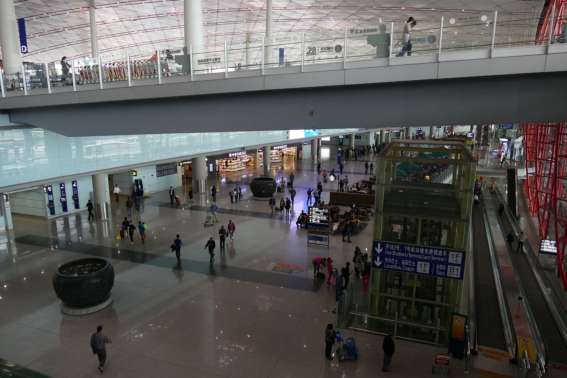A footbridge crosses the spacious concourse at Beijing Capital Airport Terminal 3, above travellers and a glass lift.
