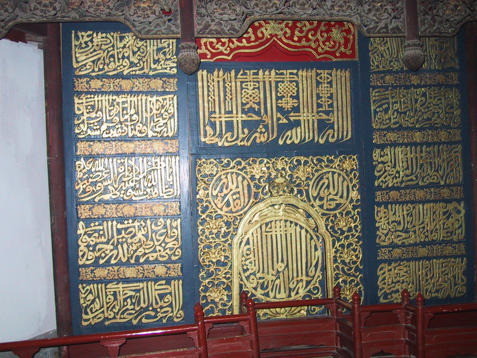 Gold Arabic calligraphy and floral patterns cover dark blue panels above a red railing inside Beijing's Niujie Mosque.